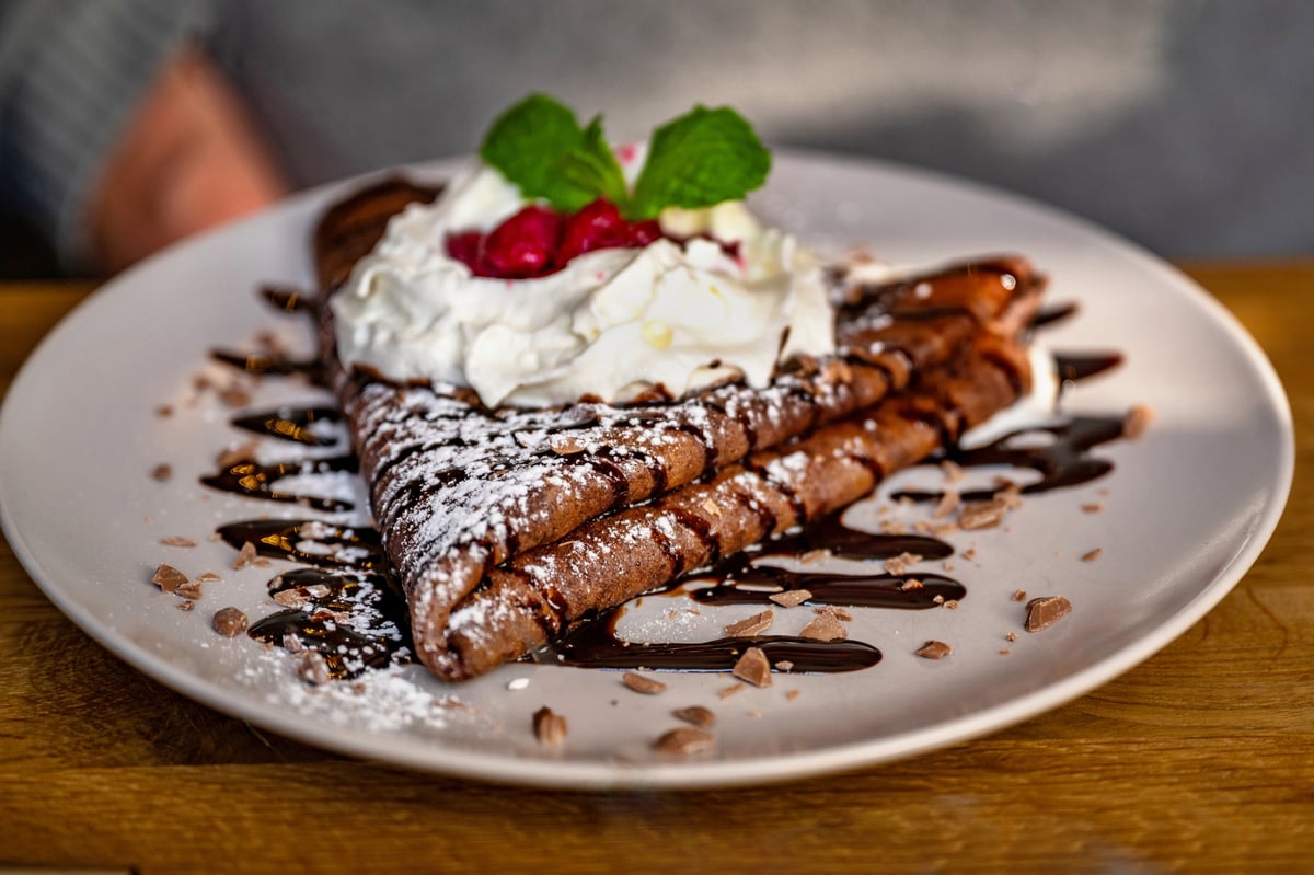 Buckwheat pancake decorated with chocolate sauce, cream and raspberry on plate.