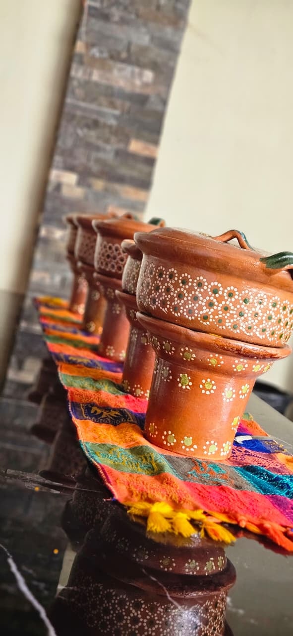 Stack of decorative wooden bowls with white dot patterns and colorful woven fabric strips on a dark surface against a cream wall