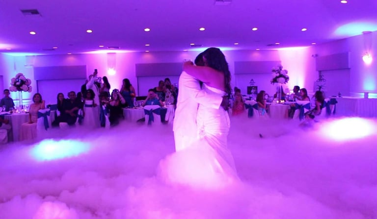 Bride and groom dancing on fog-covered dance floor with purple ambient lighting at wedding reception