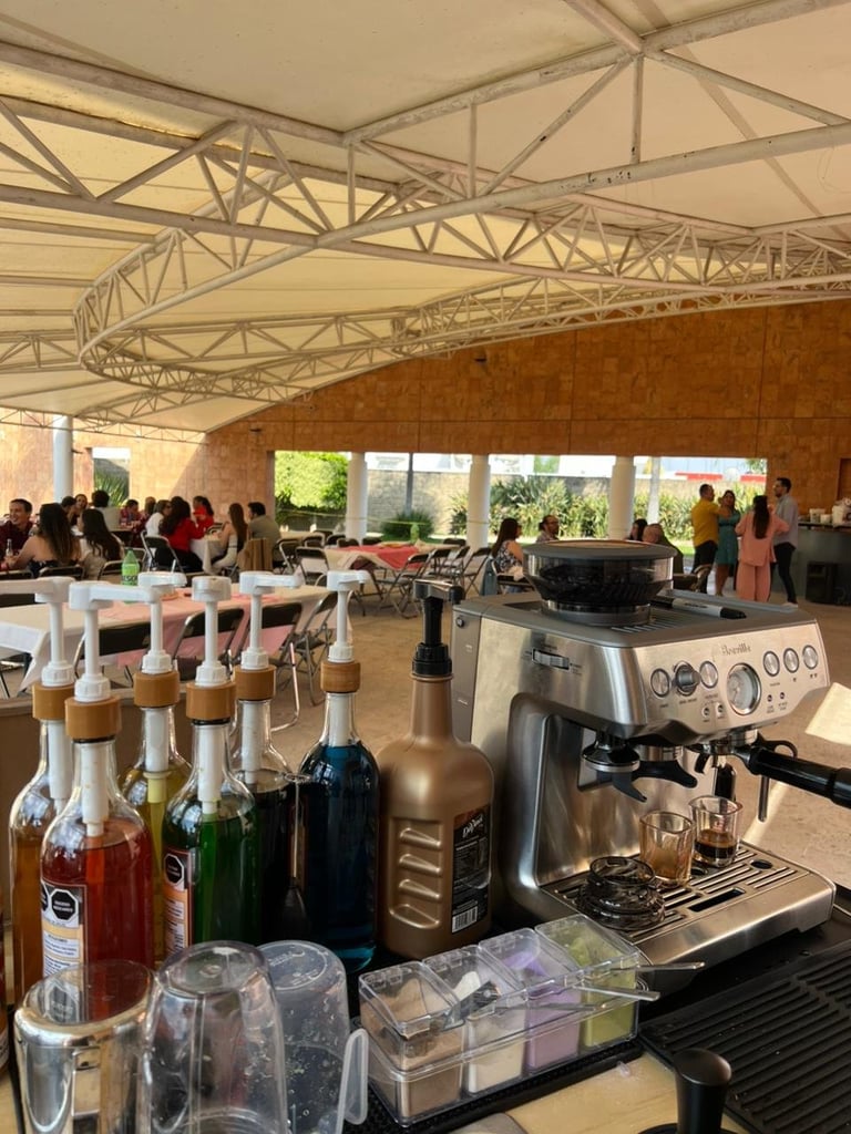Professional espresso machine and wine bottles at an indoor event venue with industrial ceiling and attendees in background